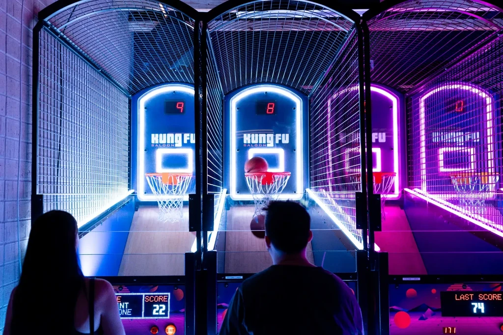 Two people at three neon-lit Kung Fu Saloon arcade games.