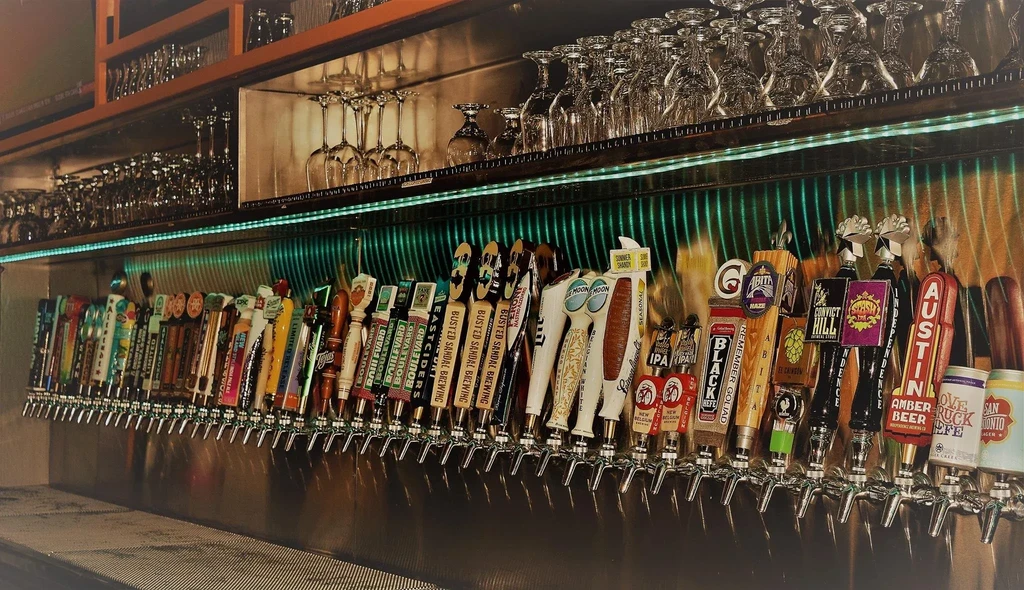 Numerous beer taps, clean glassware, and green-blue LED lighting at a bar.