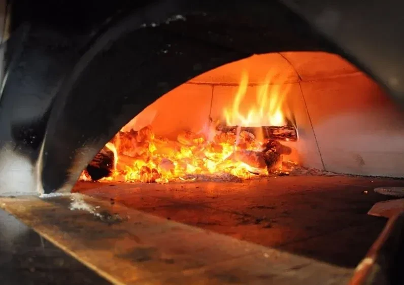 Blazing fire and glowing embers inside a heated wood-fired oven.