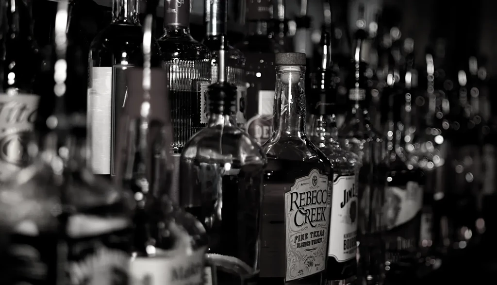 Black and white photo of liquor bottles, Rebecca Creek whiskey prominent.