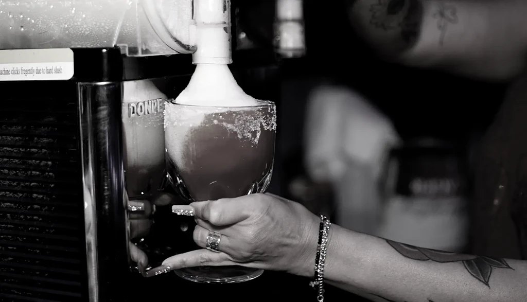 Decorated hand holds salt-rimmed glass filling with red frozen drink.