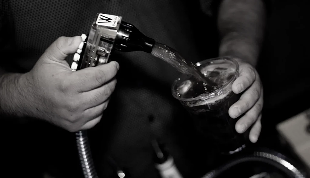 Black and white: Hands pouring drink from dispenser into iced cup.