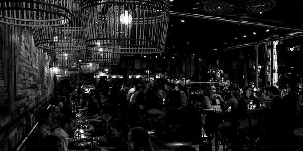 Dimly lit black and white bar or restaurant, bustling with patrons.