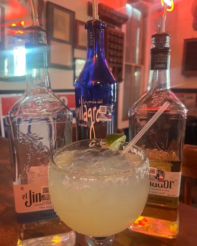 Frosty margarita with salted rim, lime, and tequila bottles.