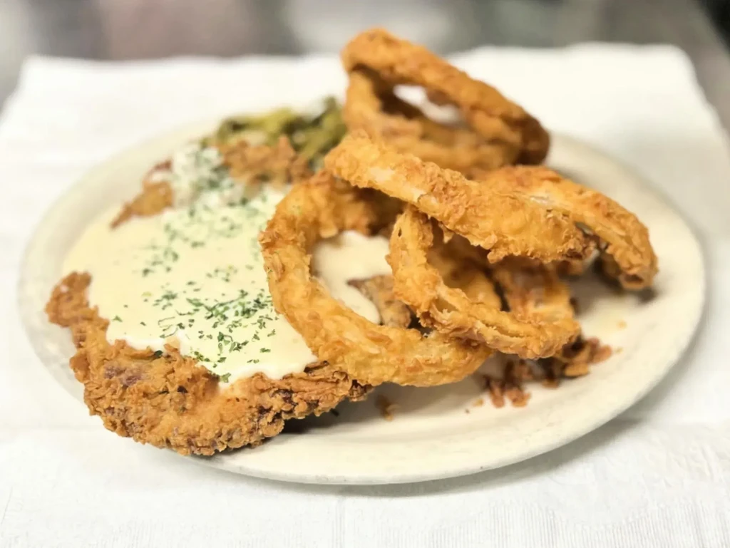 Fried cutlet smothered in gravy, topped with herbs and onion rings.