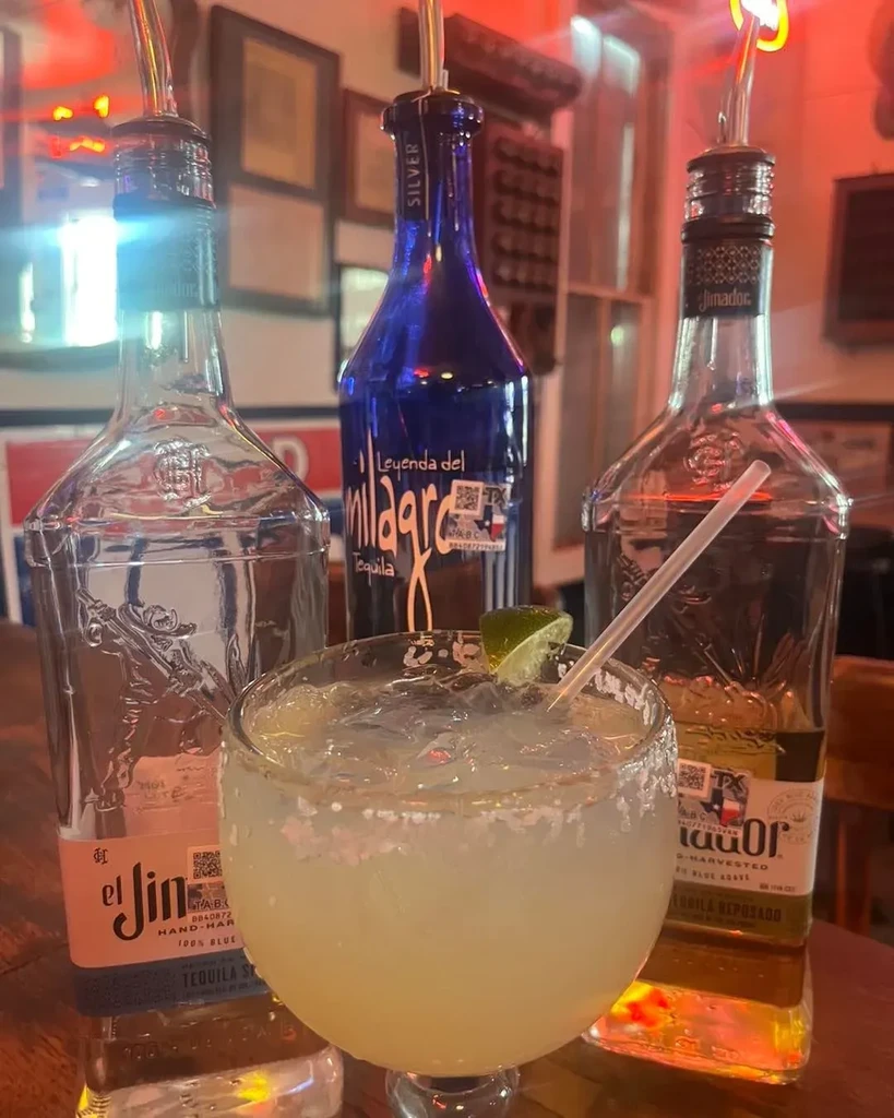 Margarita with lime, straw, ice, and three tequila bottles.