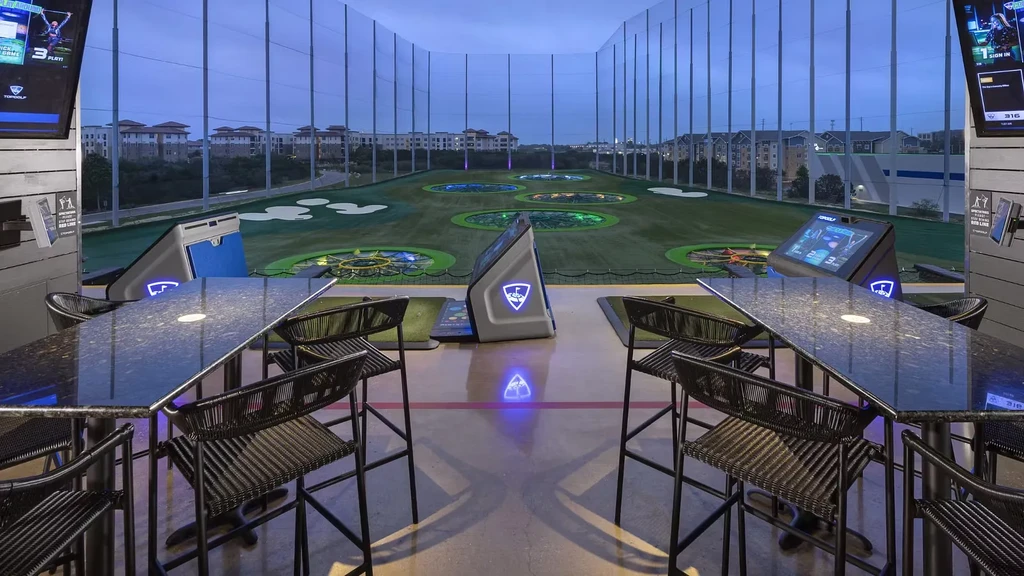 Empty modern Topgolf bay with screens facing an illuminated driving range.