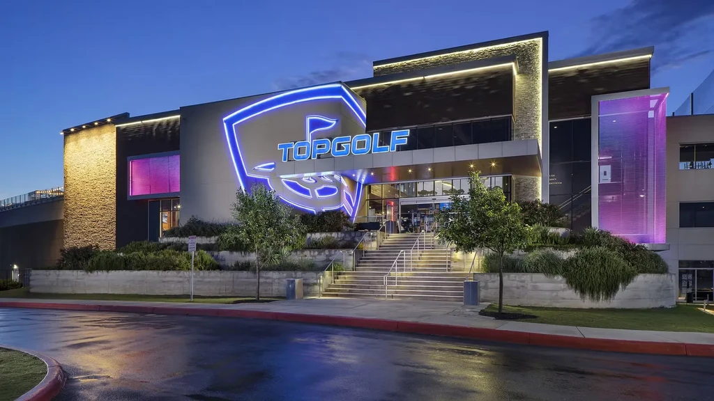 Modern Topgolf building lit at night by prominent blue neon sign.