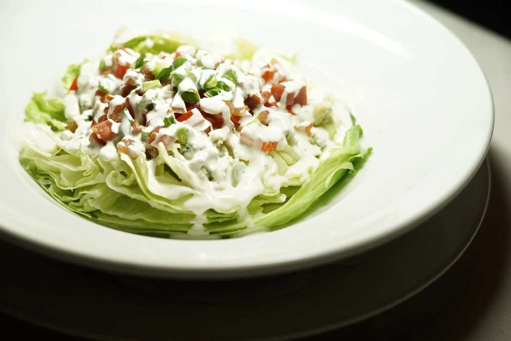 Wedge salad topped with blue cheese dressing, tomatoes, and green onions.