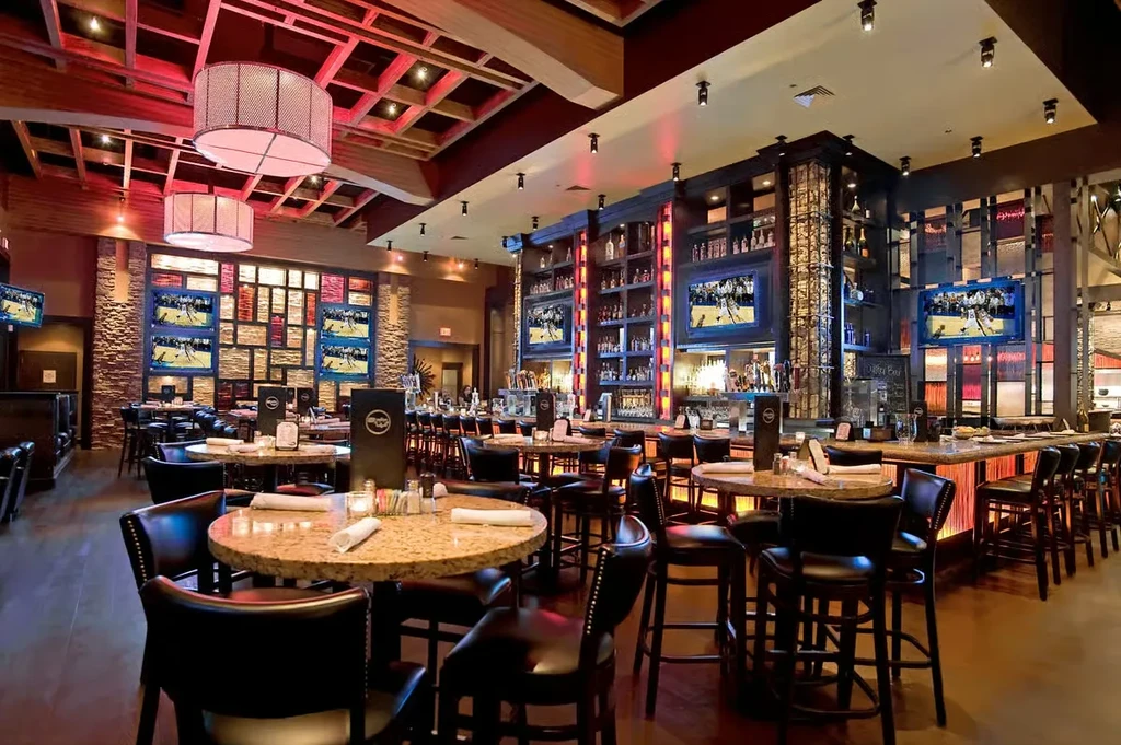 Empty, upscale sports bar with dining tables, illuminated bar, and TVs.