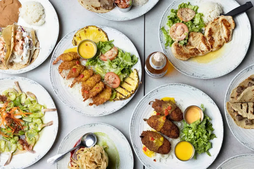 Flat lay of diverse dishes including tacos, shrimp, chicken, and Modelo.