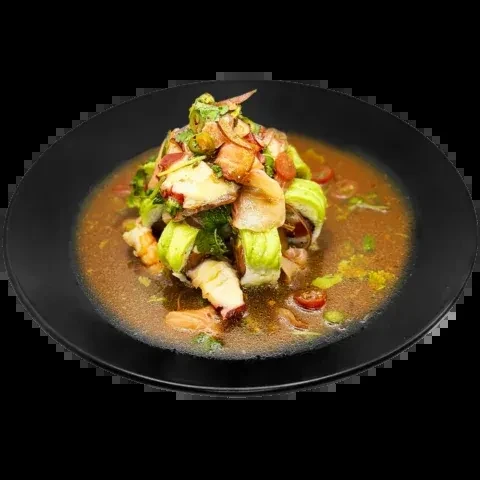 Seafood dish with octopus, shrimp, avocado, and tomatoes in a black bowl.