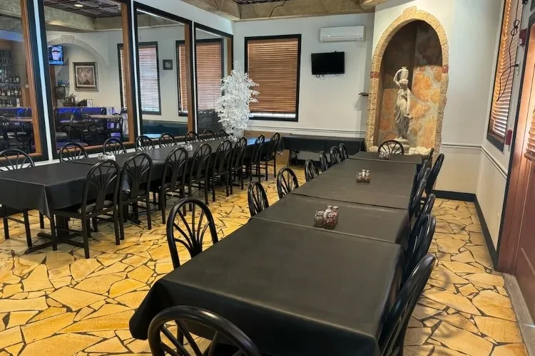 Empty restaurant dining room with dark tables, chairs, and mirrored bar.
