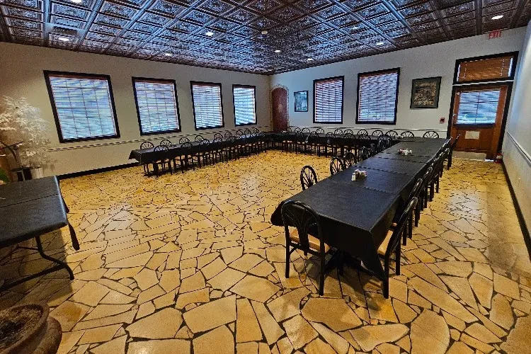 Banquet hall with U-shaped tables, black tablecloths, and ornate tin ceiling.