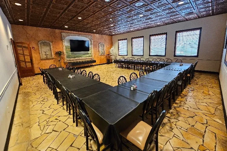 Empty private dining room with U-shaped table, stucco walls, metal ceiling.