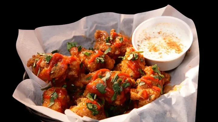Basket of red-sauced chicken bites with herbs and creamy dip.
