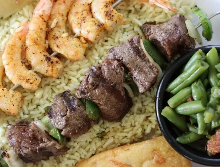Grilled shrimp and beef skewers with rice and green beans.