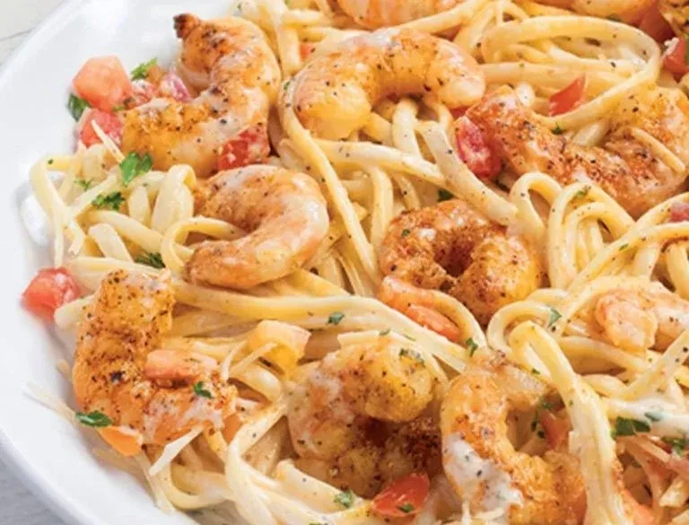 Close-up of creamy shrimp pasta with tomatoes and green herbs.