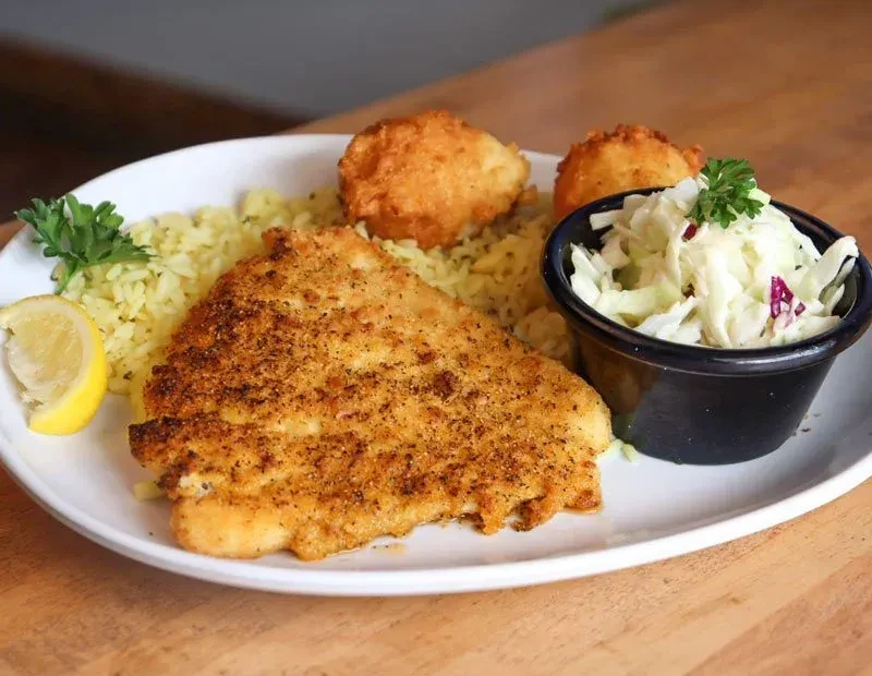 Fried fish fillet, yellow rice, hushpuppies, and coleslaw on a plate.