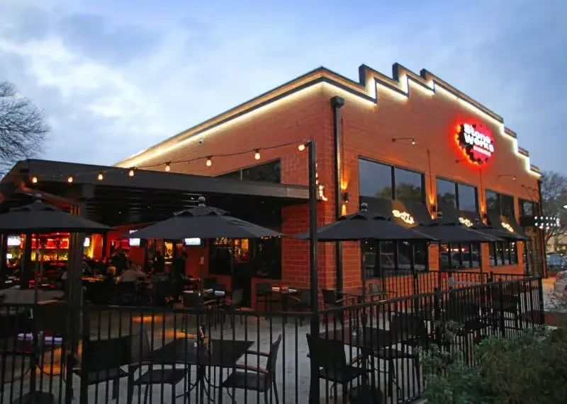 Modern brick restaurant with illuminated jagged roof, red sign, and patio.