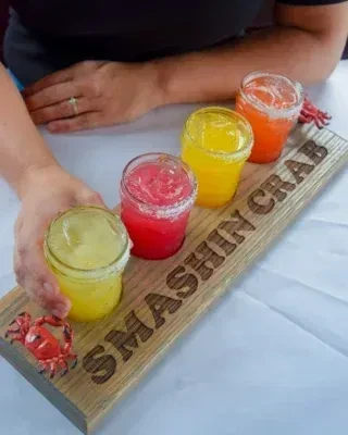 Four colorful drinks in jars on a "SMASHIN CRAB" wooden paddle.