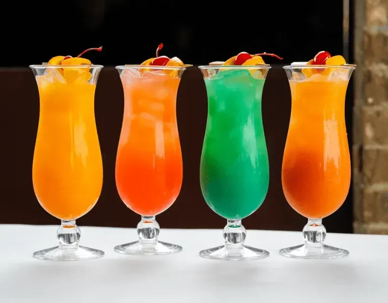 Four colorful iced drinks in garnished hurricane glasses.