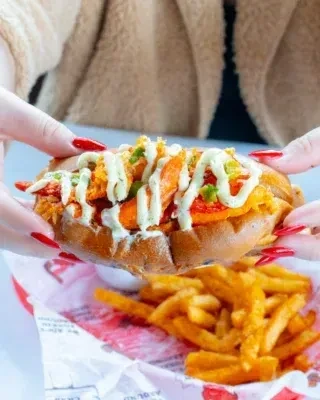 Two hands hold a generous lobster or shrimp roll over fries.