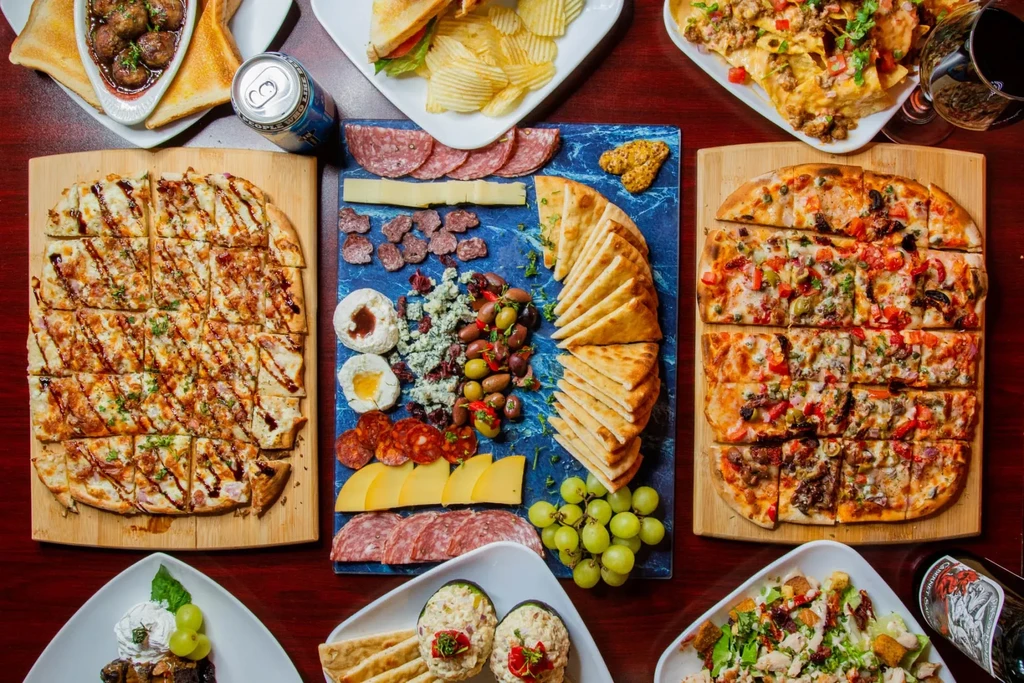 Abundant overhead spread of flatbreads, charcuterie, nachos, desserts, and drinks.