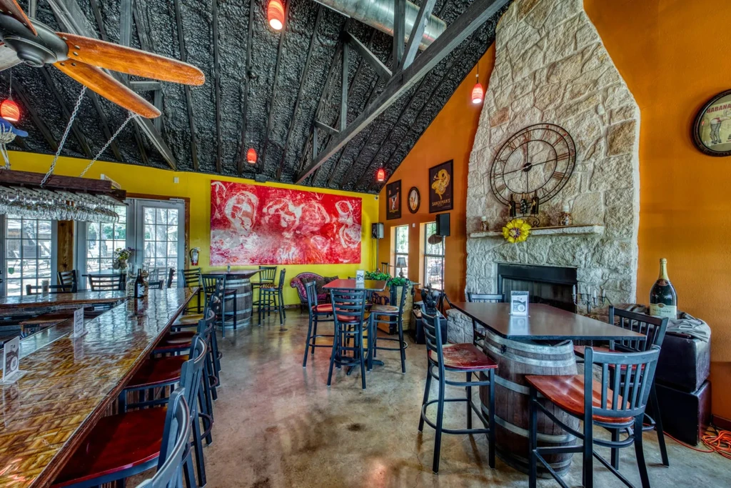 Vibrant, eclectic restaurant interior with bar, stone fireplace, and barrel tables.