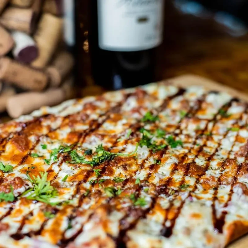 Rectangular pizza with white cheese, dark drizzle, green herbs on wood.