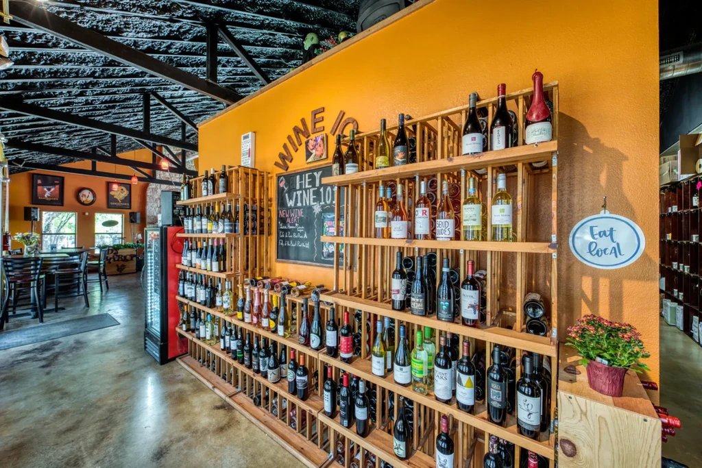 Rustic wine bar interior with shelves of bottles and dining area.