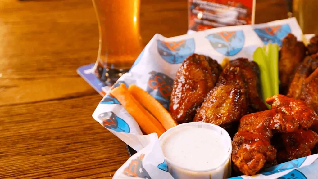 Basket of sauced chicken wings, carrot, celery, creamy dip, and beer.