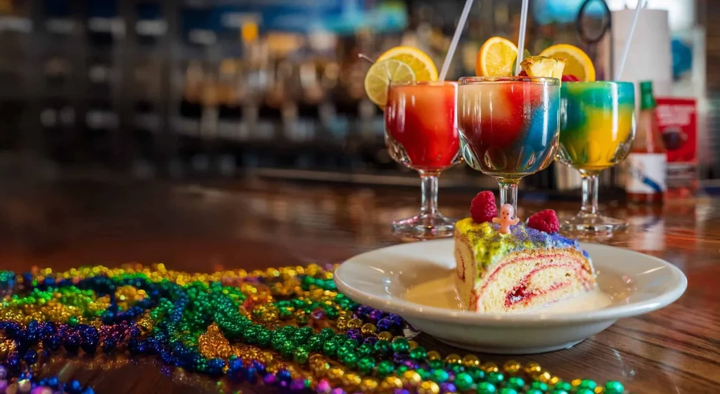 Mardi Gras King Cake, colorful beads, and layered frozen drinks on a bar.