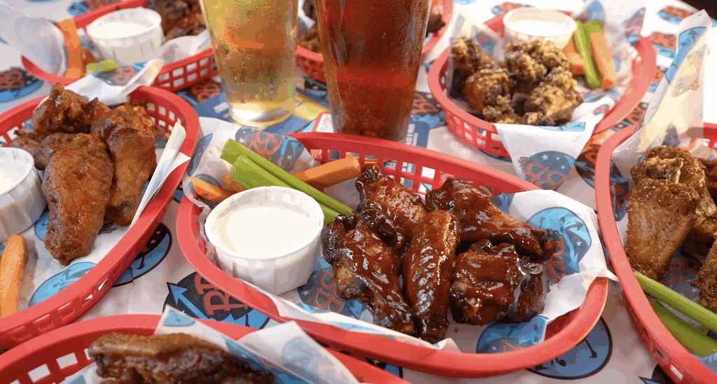 Multiple baskets of chicken wings, sauces, vegetable sticks, and beverages.
