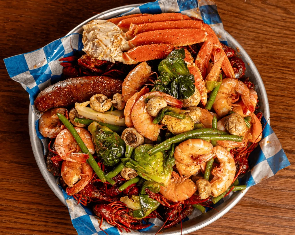 Colorful seafood boil platter with shrimp, crab legs, crawfish, and vegetables.
