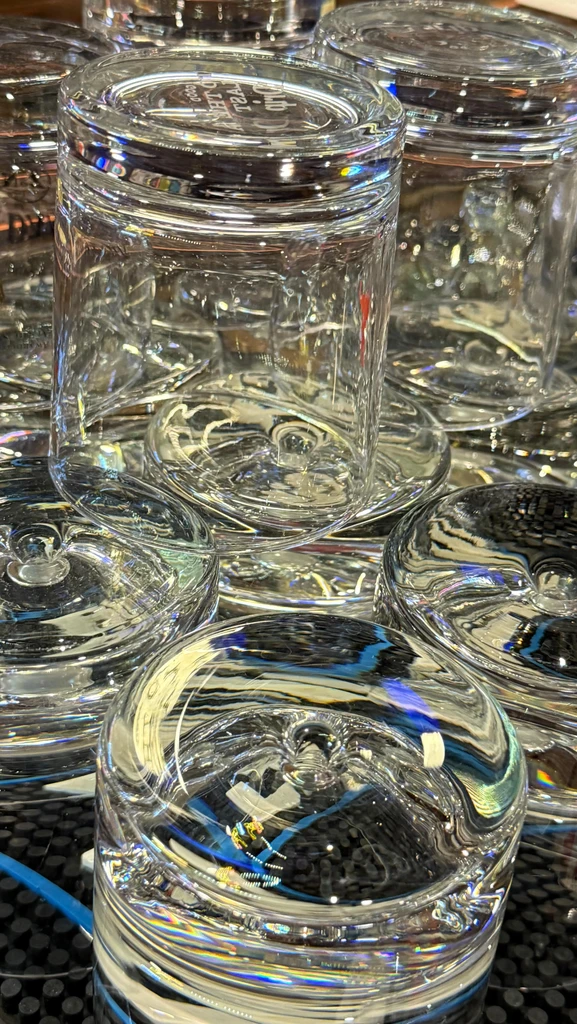 Empty clear glass tumblers reflecting colorful light on a black bar mat.