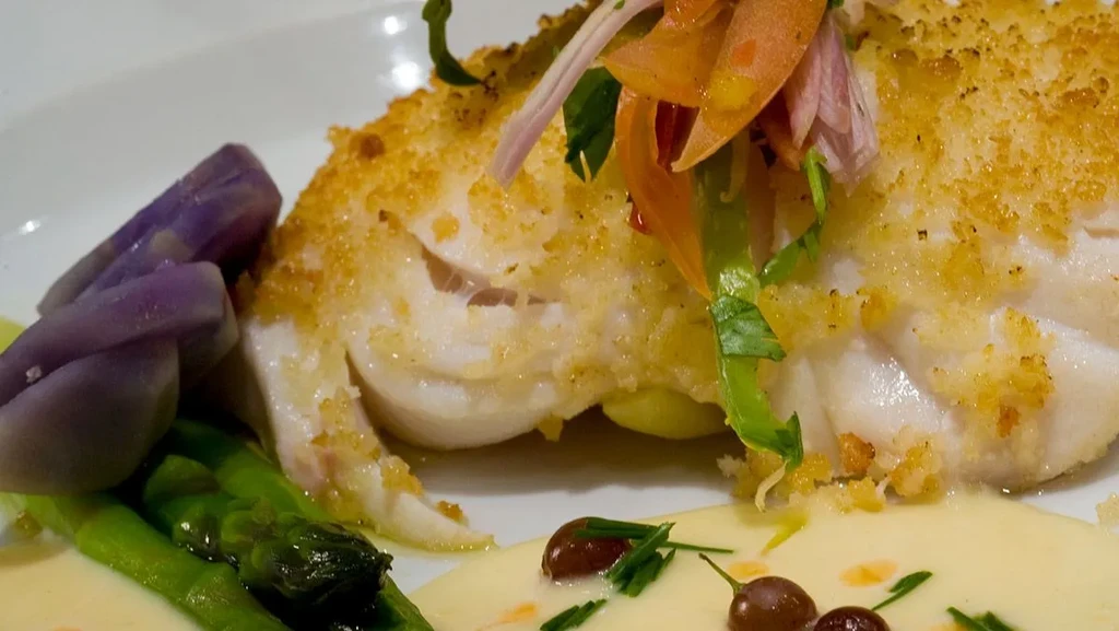 Crispy breaded white fish, asparagus, purple potatoes, garnished with herbs and sauce.