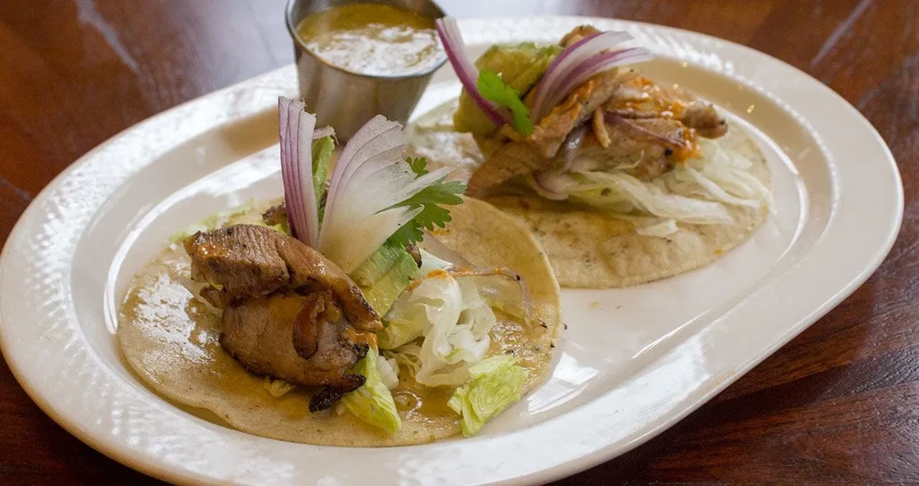 Two soft corn tacos filled with meat, lettuce, onion, cilantro.