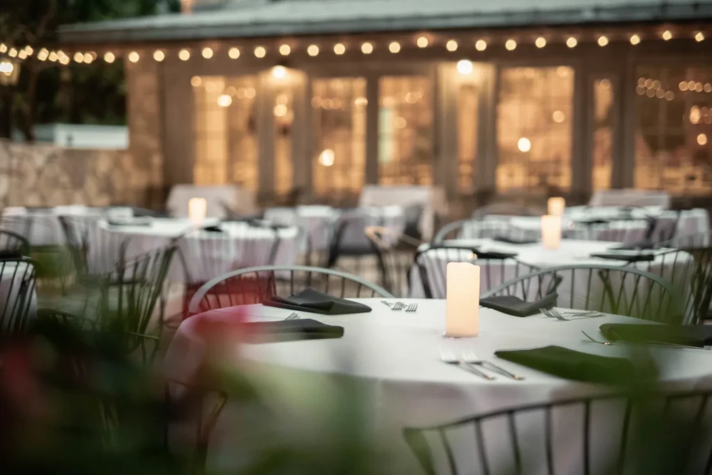 Outdoor dining tables meticulously set with glowing centerpieces at night.