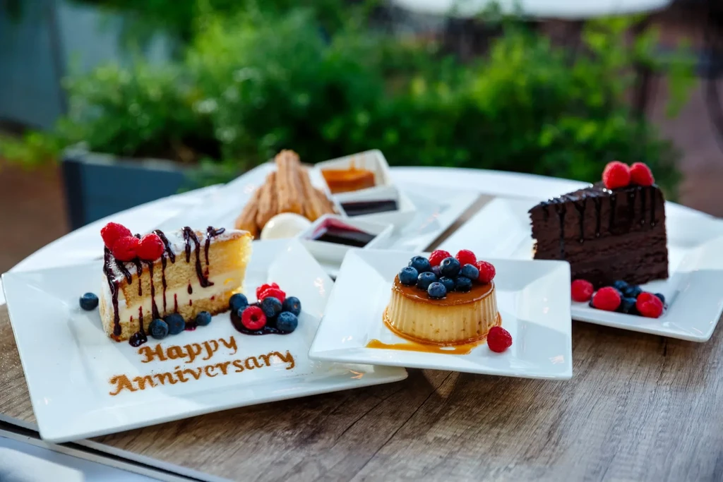 Happy Anniversary cakes, flan, and churros on a rustic table.