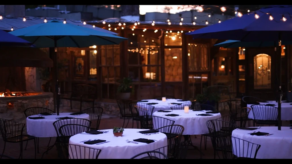 Outdoor restaurant patio with candlelit tables, string lights, and fire pit.
