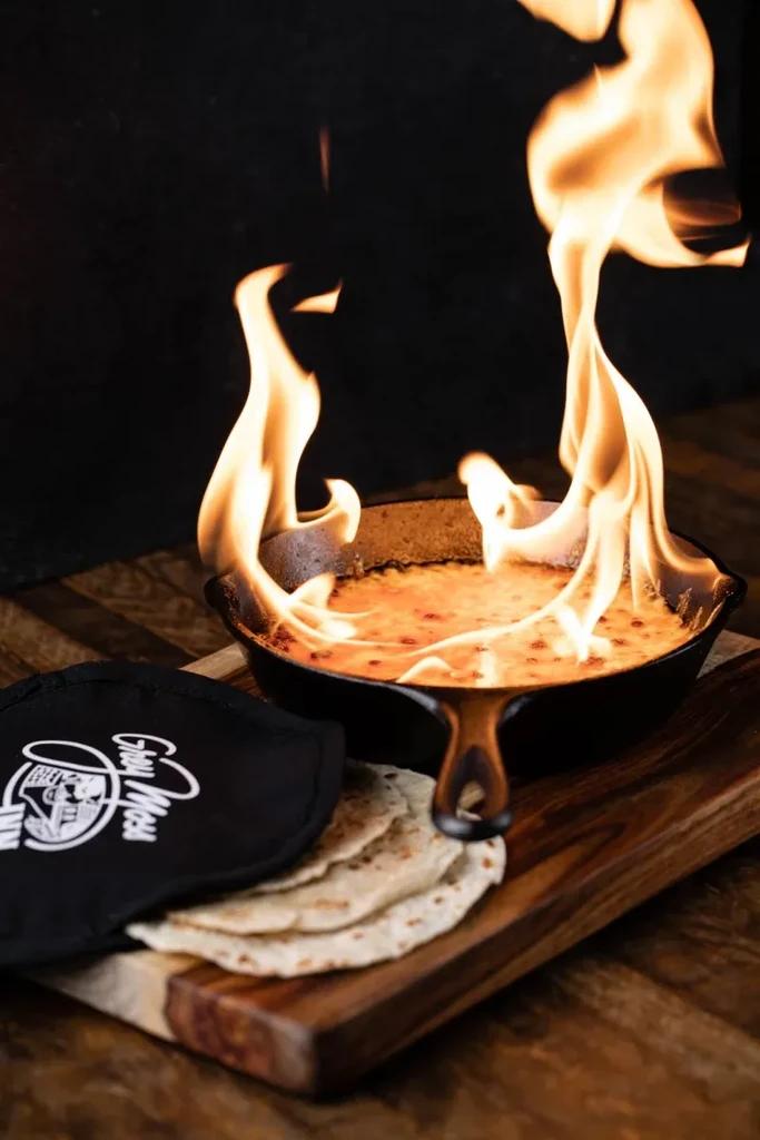 Bubbling, flaming cheesy dip in a skillet, with tortillas.