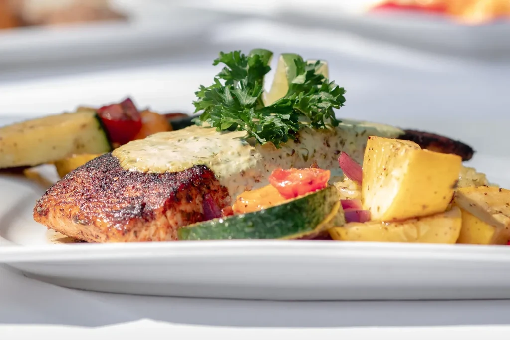 Plated seared fish with green sauce, lime, and roasted vegetables.