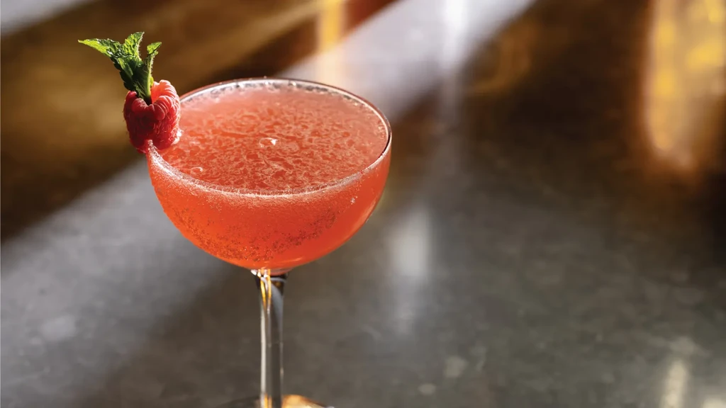 Effervescent pink cocktail in coupe glass with raspberry and mint.