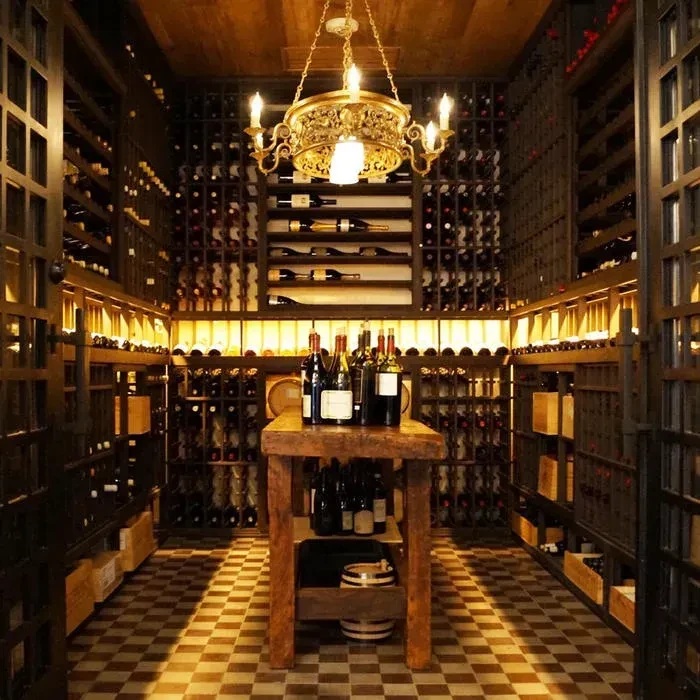 Ornate wine cellar with rows of bottles, table, and chandelier.