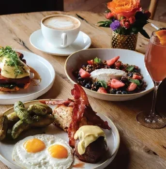 Varied brunch spread with eggs, bacon, yogurt, coffee, and a cocktail.