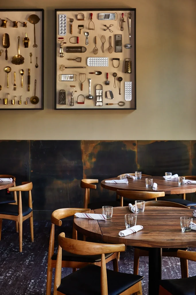 Empty restaurant dining room with wooden tables, chairs, and vintage utensil displays.