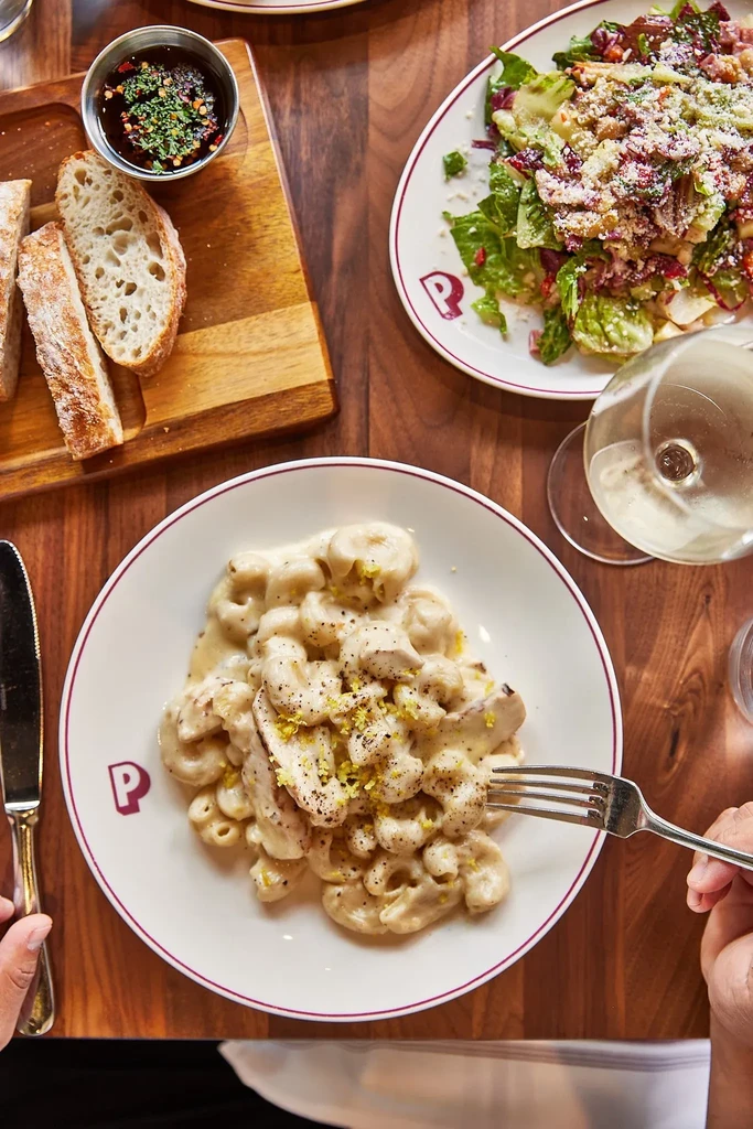 Overhead: Person's hands poised to eat pasta, salad, bread, and wine.