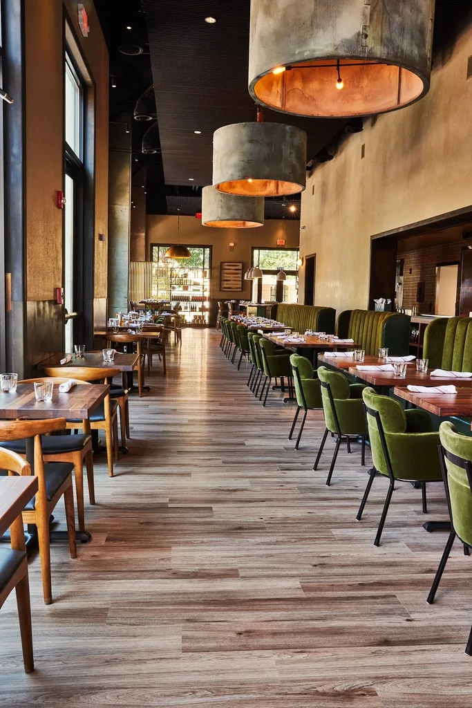 Empty, stylish restaurant interior with olive green banquettes and industrial lighting.