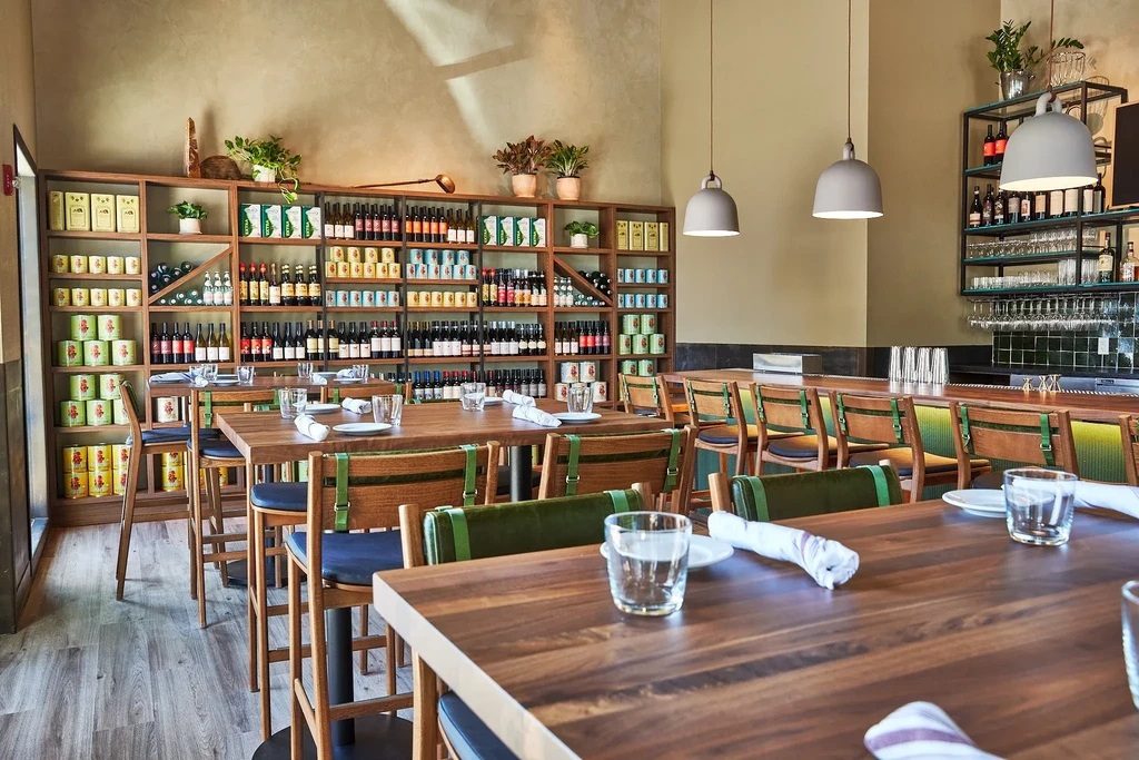 Modern restaurant interior with dining tables, bar, and retail shelving.